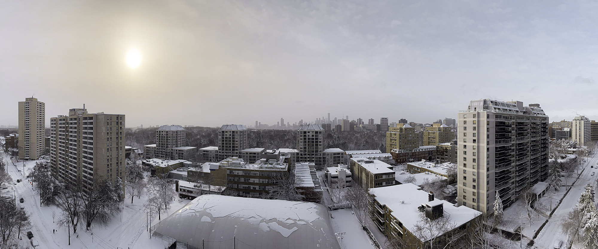 March 4, 2023 at 8:35 AM - Wide winter panorama of Midtown Toronto at dawn: soft pale sun hangs in a misty sky, every rooftop, street, and tree blanketed in fresh snow, with the distant skyline fading into the haze