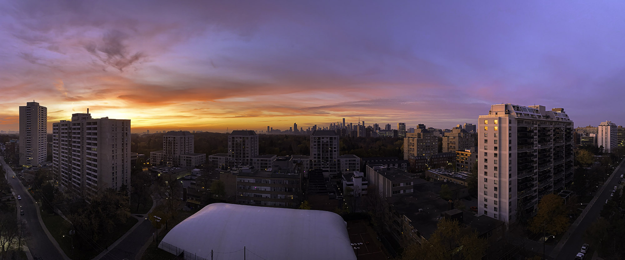November 15, 2023 at 6:56 AM - Fiery sunrise over Midtown Toronto: intense bands of pink, orange, and violet sweep the sky, illuminating silhouetted buildings and bare November trees