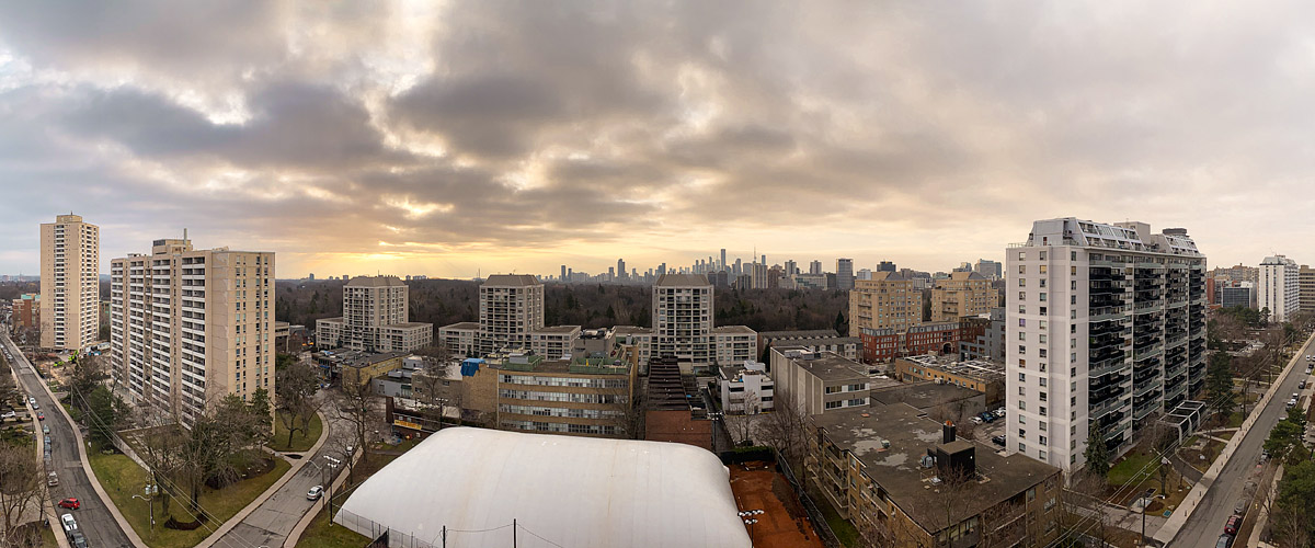 Heavy layered grey cloud fills the sky with a band of pale gold light along the horizon behind the skyline, the ground bare and the courts under their pale dome.