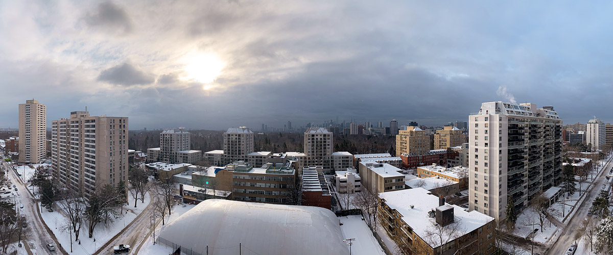 A thick grey cloud layer with the sun showing as a bright disc through it, the skyline dark and low in contrast, snow across the ground.