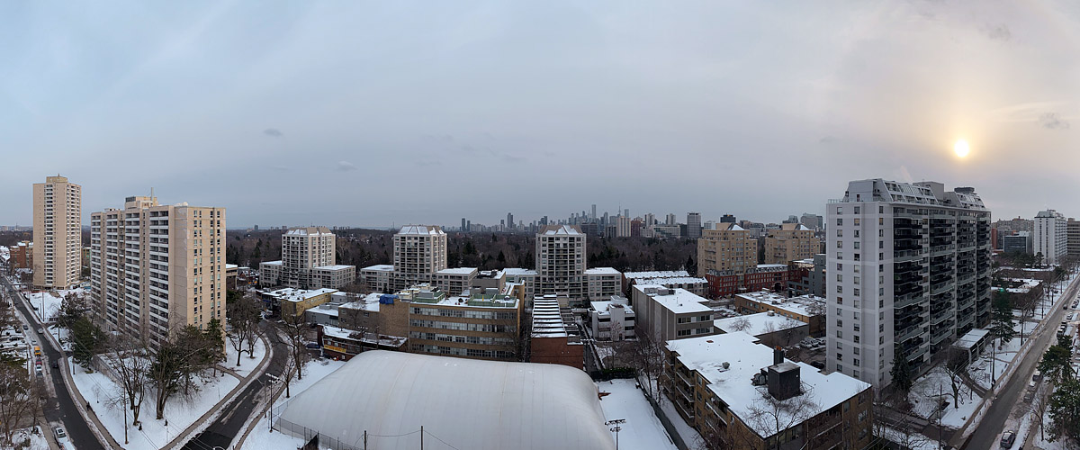 Flat pale grey cloud covers the whole sky with a weak white sun low to the right, the skyline faint, snow lying below.