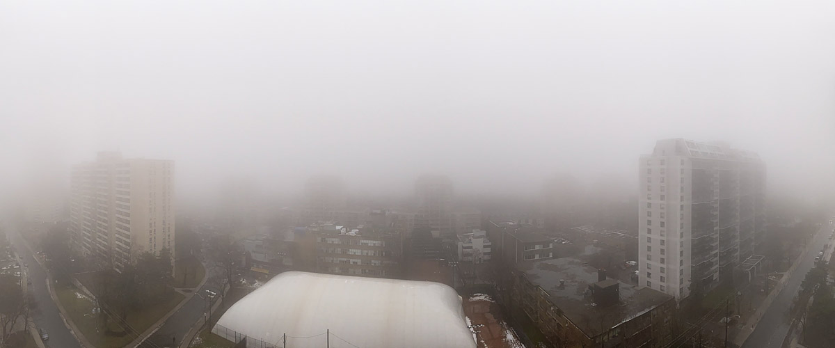 Thick fog erases the skyline and softens the nearest towers to outlines, the ground wet and dark with patches of snow.