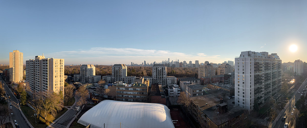 Open blue sky with a few thin wisps of cloud near the horizon and a low sun to the right, the ground bare and the clay courts showing beside the dome.