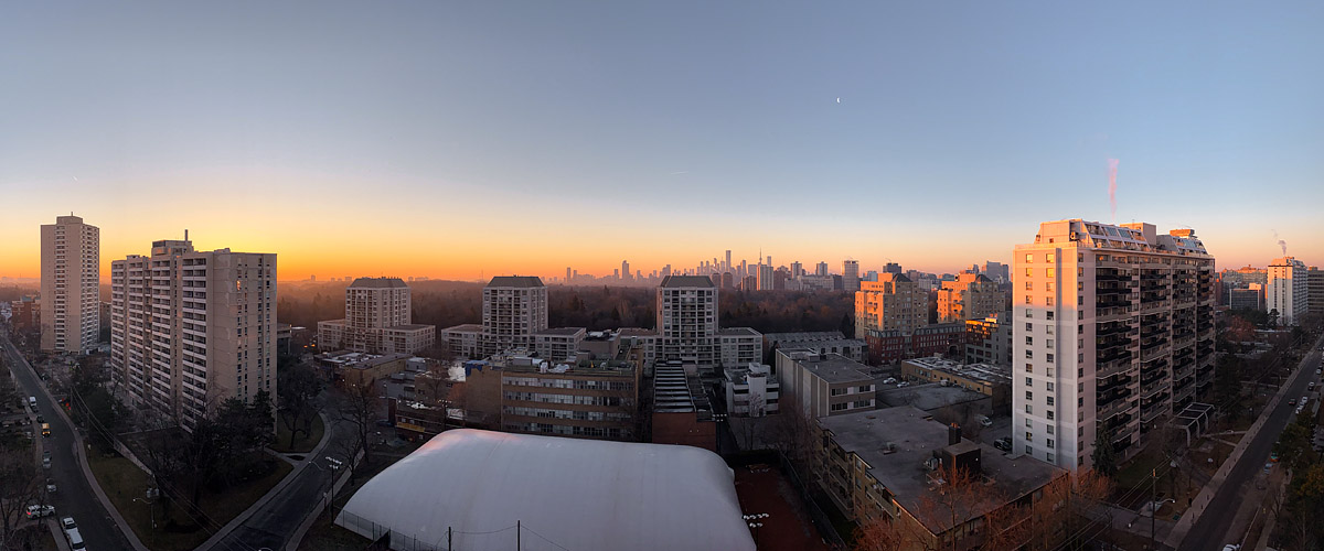 A clean orange to blue gradient before sunrise with a thin crescent moon high above the skyline, the ground bare.