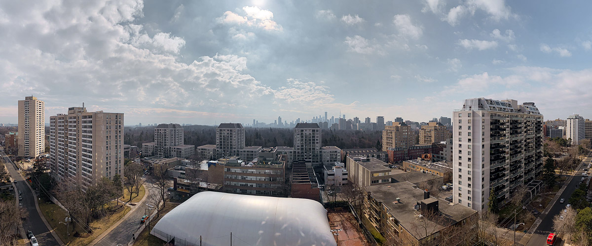 Large white and grey cloud with blue between, the sun hidden behind cloud overhead and the skyline soft in the distance.