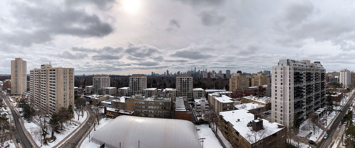 A textured grey cloud deck covers the sky with the sun a soft bright patch above, the skyline legible and the ground white with snow.