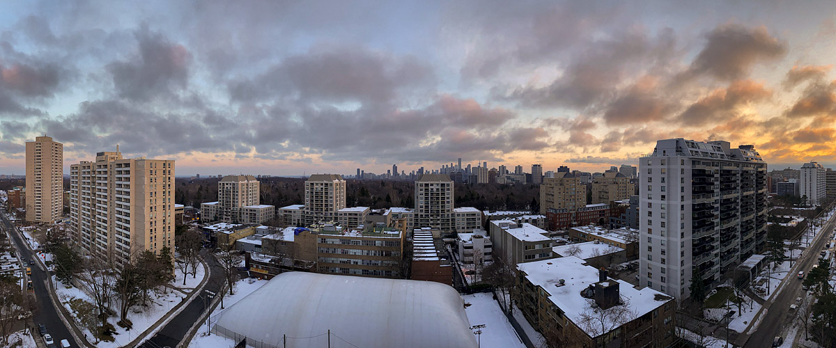 Broken grey cloud with pink and gold underlight and a bright break to the right, snow lying on the roofs and ground.