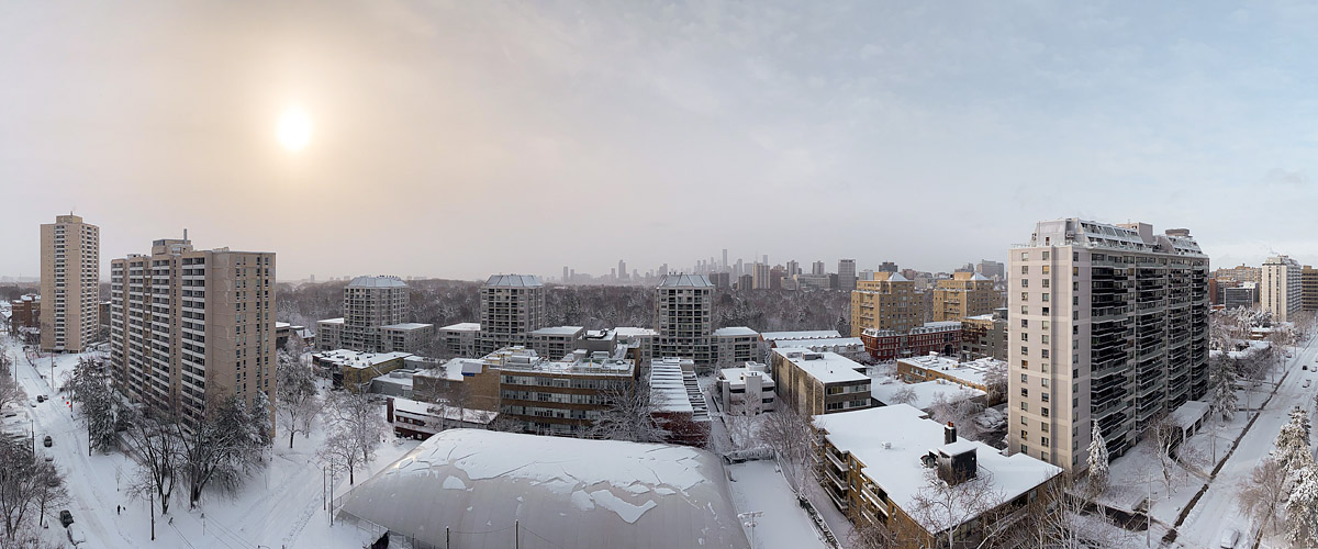 The sun is a soft disc in milky air, the skyline a faint outline nearly lost in the haze, deep snow on every roof and branch.
