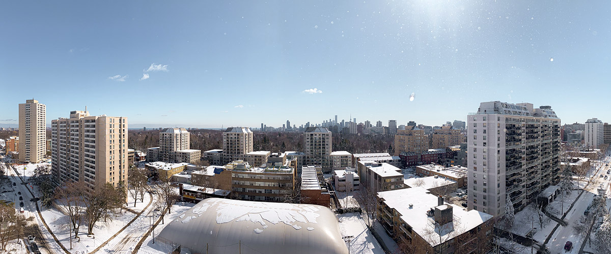 Deep blue sky with a high bright sun and a few small clouds at the horizon, snow lying white across the whole scene.