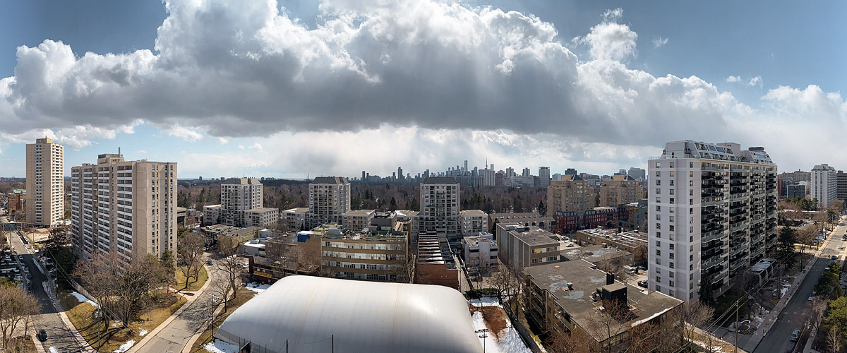 Tall white cumulus with dark bases across a blue sky, the skyline sharp beneath them and old snow in patches on the grass.