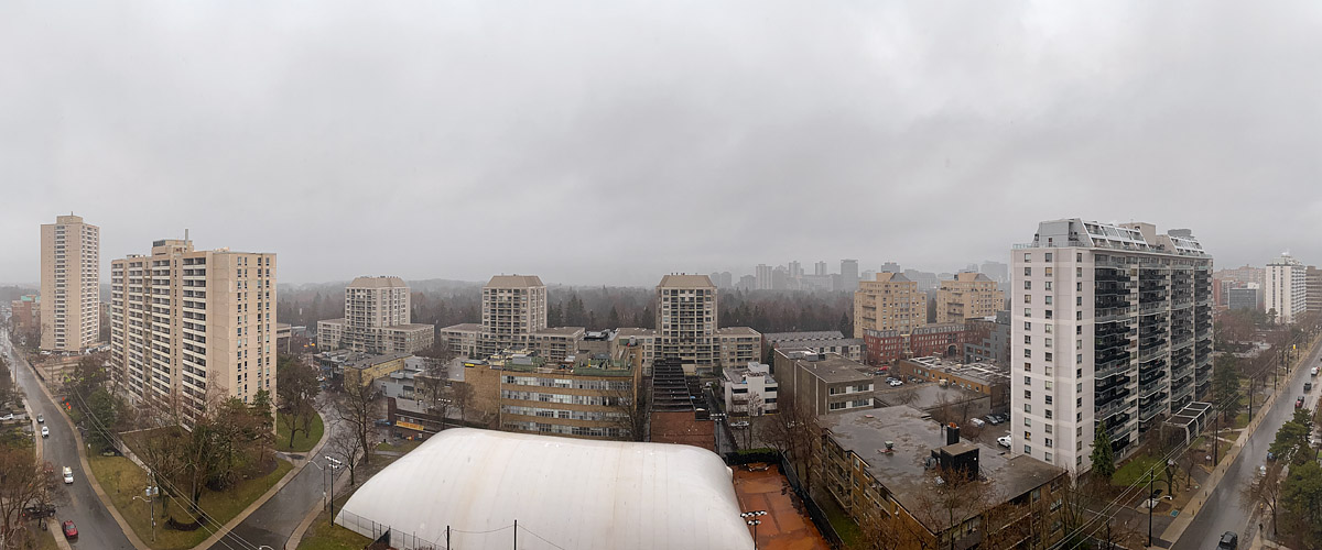 Uniform grey cloud with rain falling, the skyline pale and low in contrast and the streets wet below.