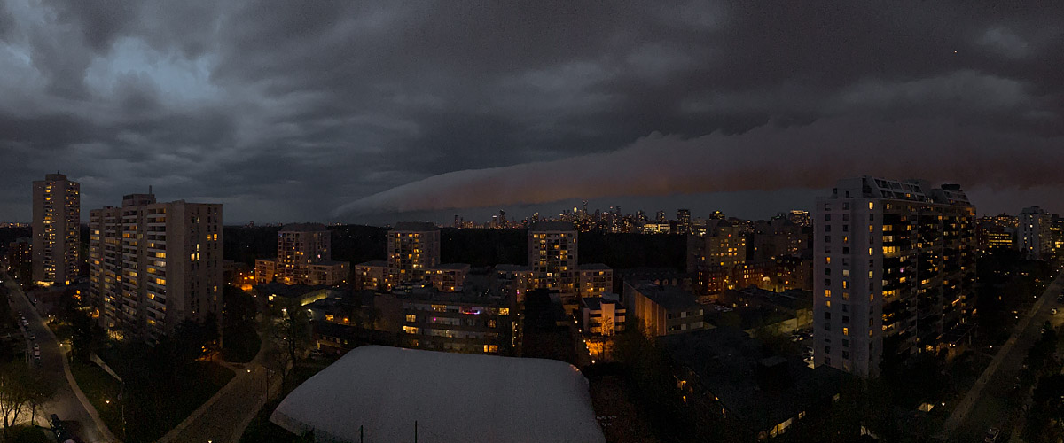 A dark shelf of storm cloud runs the width of the sky with a copper glow beneath it and the city lit below.