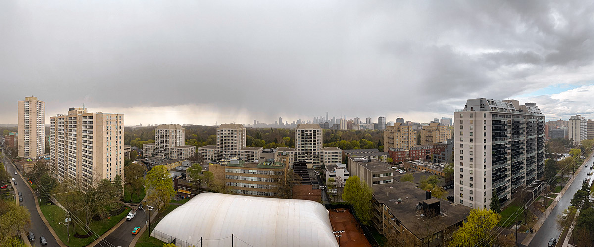 A grey cloud deck with rain falling in shafts over the downtown towers, the skyline soft behind the curtain.