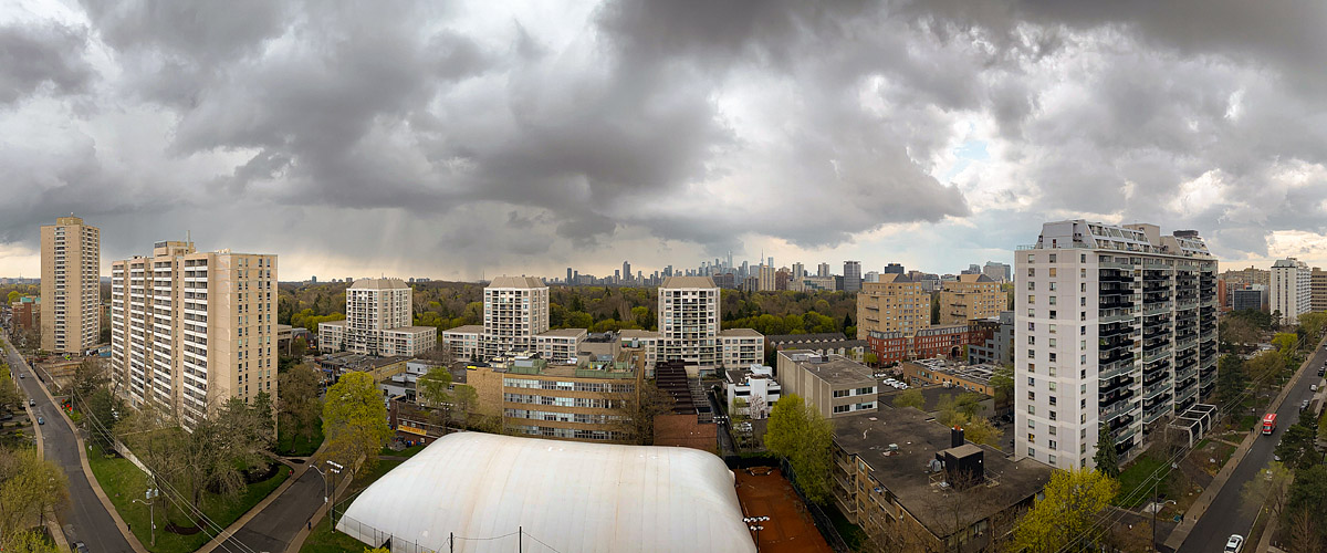 Broken heavy cloud with brighter gaps and rain trailing over the city, the skyline grey in the distance.