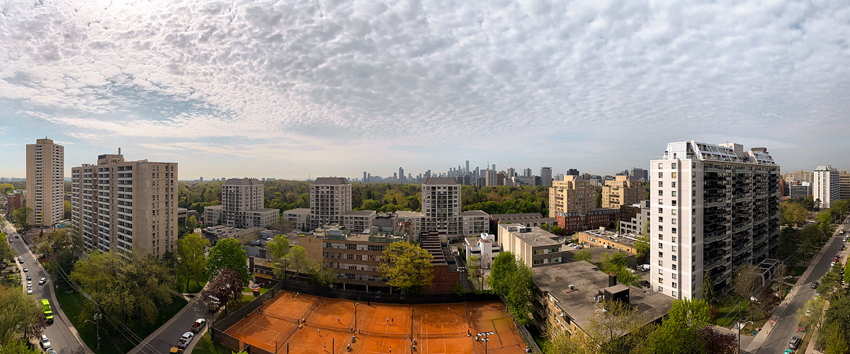 A rippled deck of small clouds covers the upper sky with clear blue at the horizon, the clay courts open below.