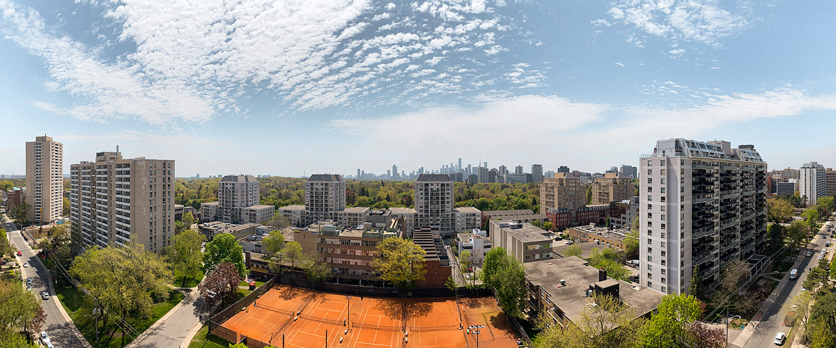 Patches of small white cloud across a blue sky with the skyline sharp and the clay courts busy below.