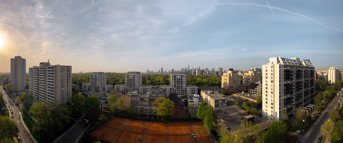 Clear pale sky with the low sun to the left and thin contrails overhead, the skyline soft in warm light.