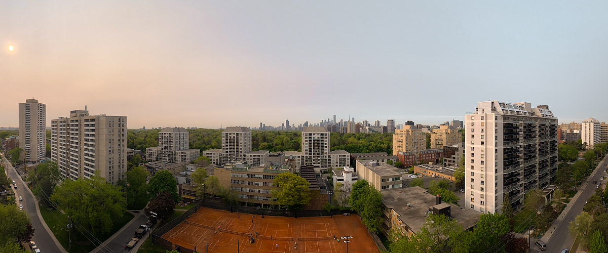 Smoke haze turns the sky milky pink and reduces the sun to a pale orange disc, the skyline faint behind it.