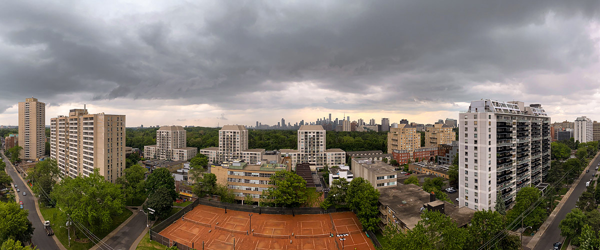 Dark storm cloud fills the sky from edge to edge with a narrow band of pale light along the horizon behind the skyline.