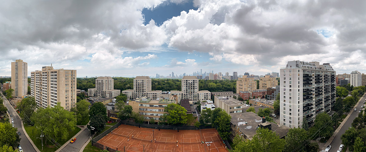 Grey and white cumulus break across a blue sky with the skyline soft behind them and the clay courts open below.