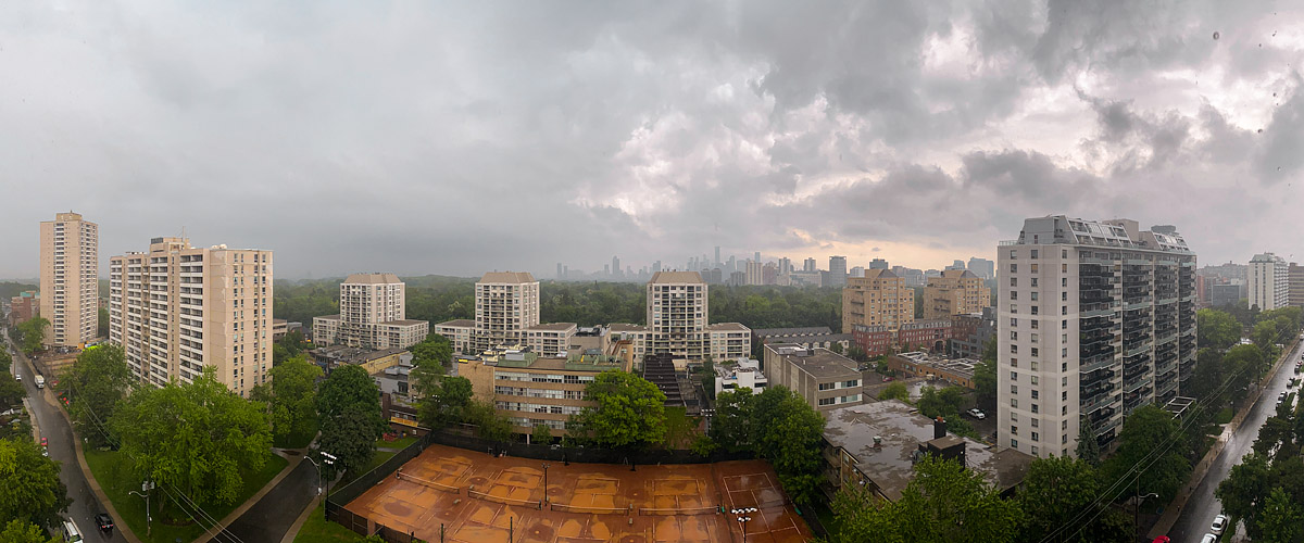 A grey rain cloud deck with a warm break at the right horizon, the skyline pale and the courts wet below.
