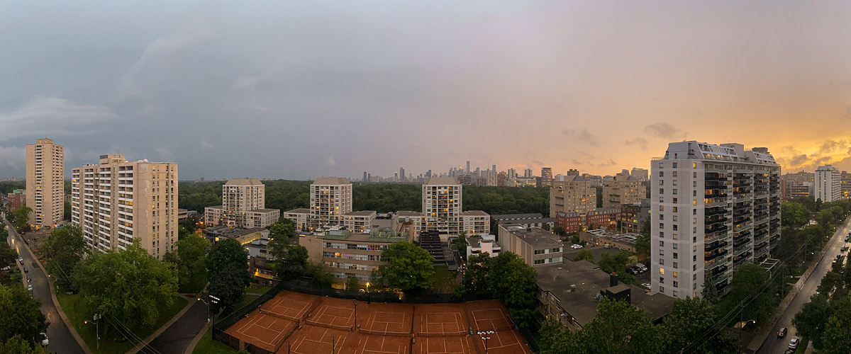 Heavy grey rain cloud with an orange break at the right horizon and the courts lit warm below.
