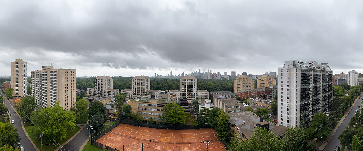 A dark grey cloud deck with rain, the skyline legible in flat light and the clay courts wet and empty.