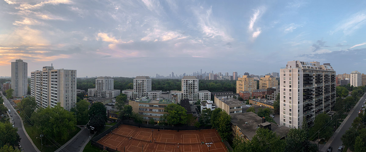 Soft mauve and peach cloud covers the whole sky with a warm glow at the left horizon, the skyline faint in haze and the courts empty below.
