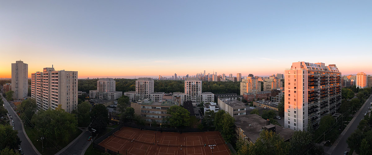 Clear sky before sunrise with a peach glow along the horizon and blue above, the skyline sharp in silhouette.