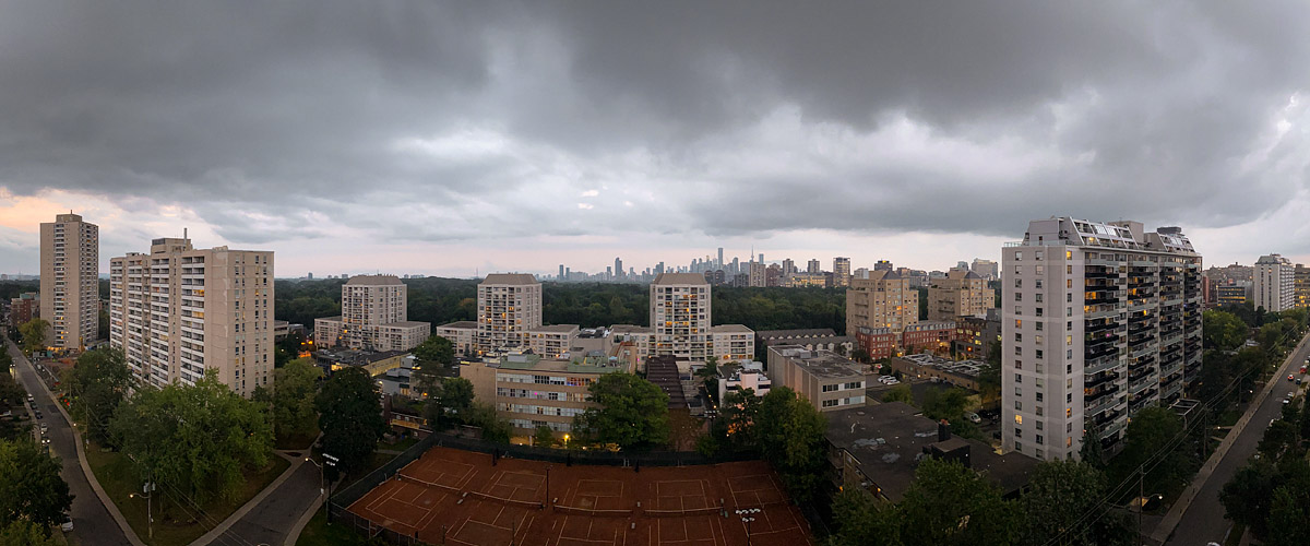 A heavy dark cloud deck fills the sky with a pale band along the horizon and the city lights on.