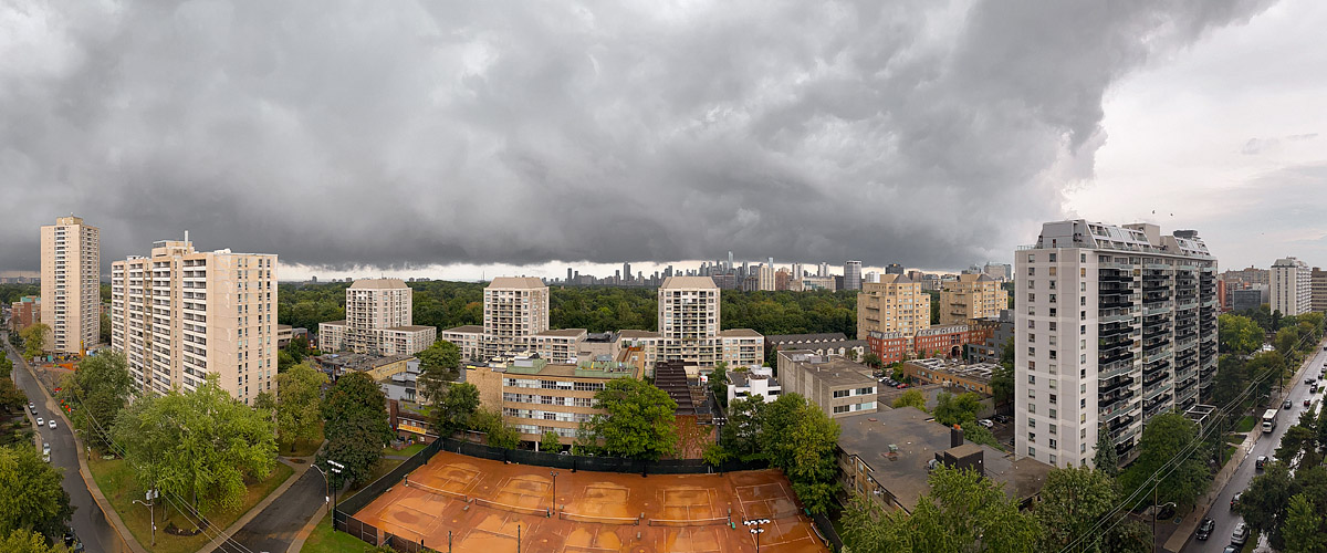 A dark storm front with a hard leading edge above the skyline and sun on the courts.