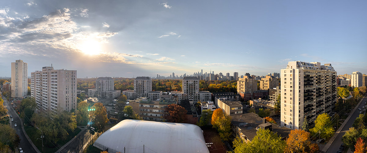 The sun sits behind broken cloud on the left with clear blue to the right and autumn colour below.