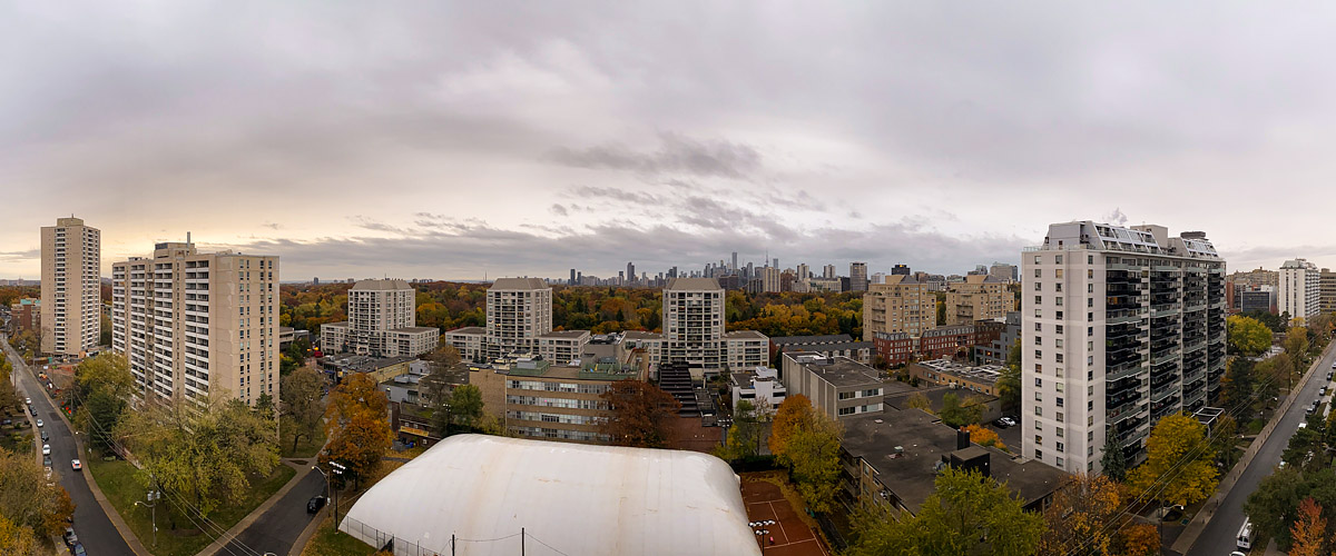 Uniform grey cloud with a narrow warm break at the far left horizon, the skyline legible in flat light.