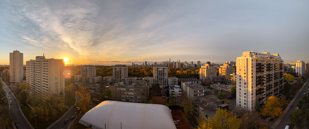 Thin cloud over a pale sky with the sun just above the horizon at the left and a gold band behind the skyline.