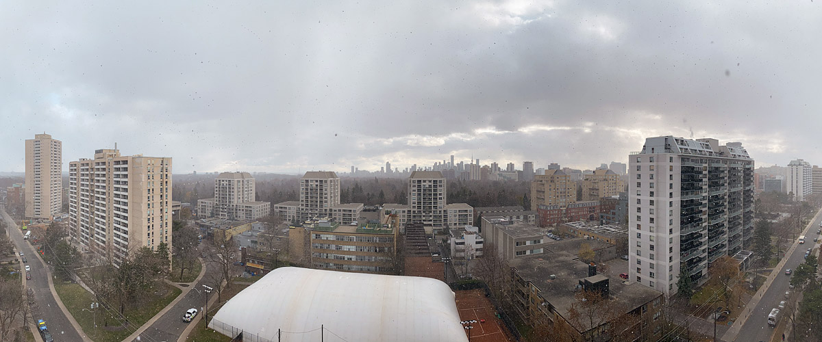 Flat grey cloud in rain with drops on the glass, the skyline soft and the trees bare below.