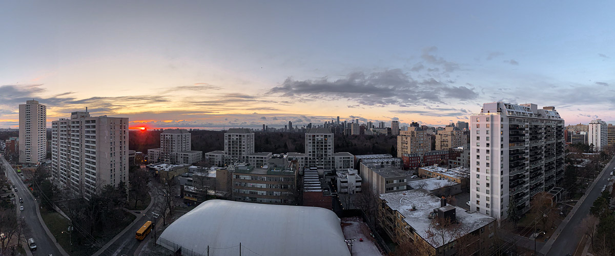 Dark cloud streaks across a pale sky with the sun a red disc on the horizon and snow on the rooftops.