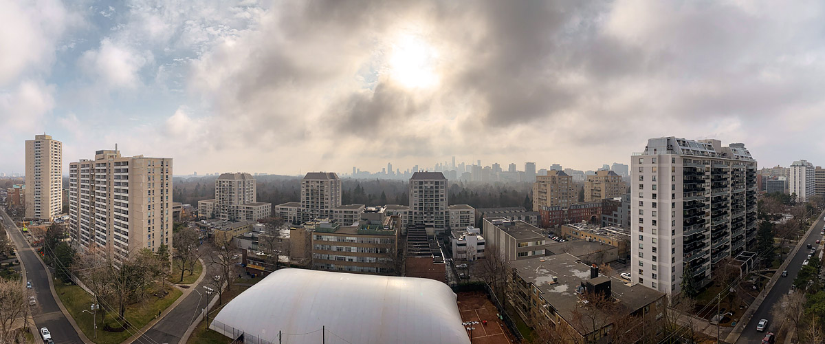 Broken cloud with the sun bright through a gap overhead, the skyline soft behind the haze.
