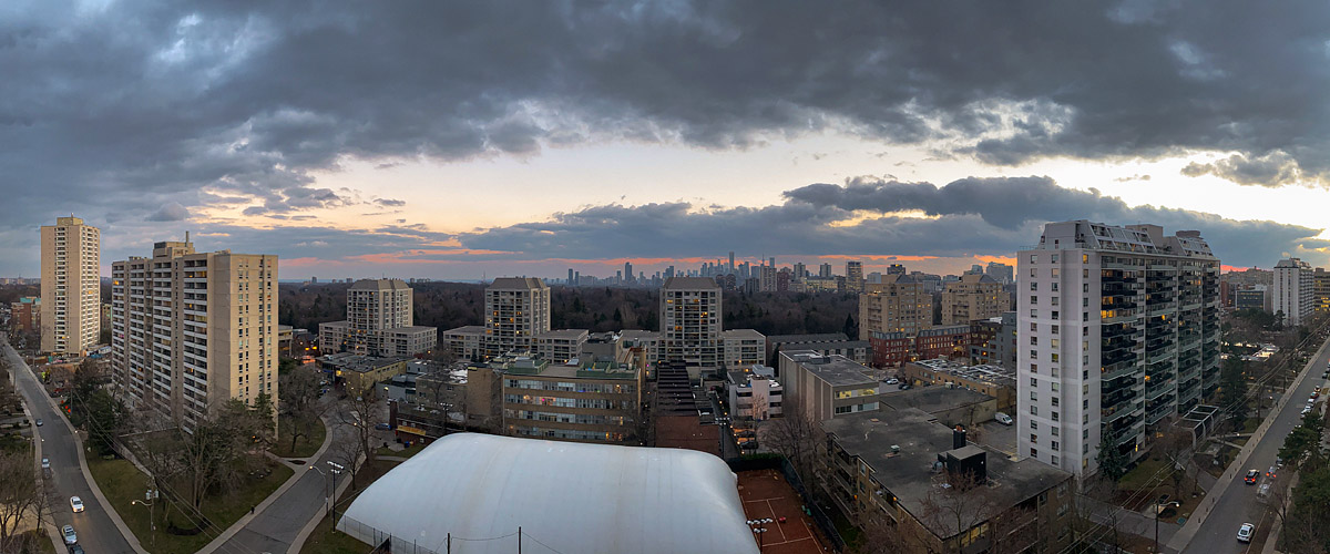 A dark broken cloud deck with a peach band of light along the horizon and the city lights on.