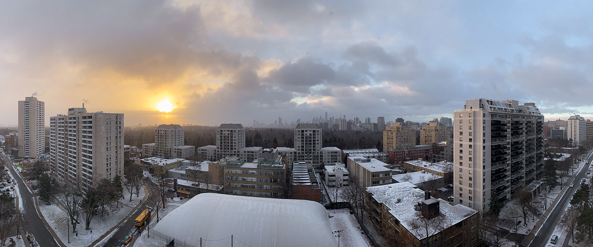The sun breaks through heavy broken cloud on the left over a scene covered in fresh snow.