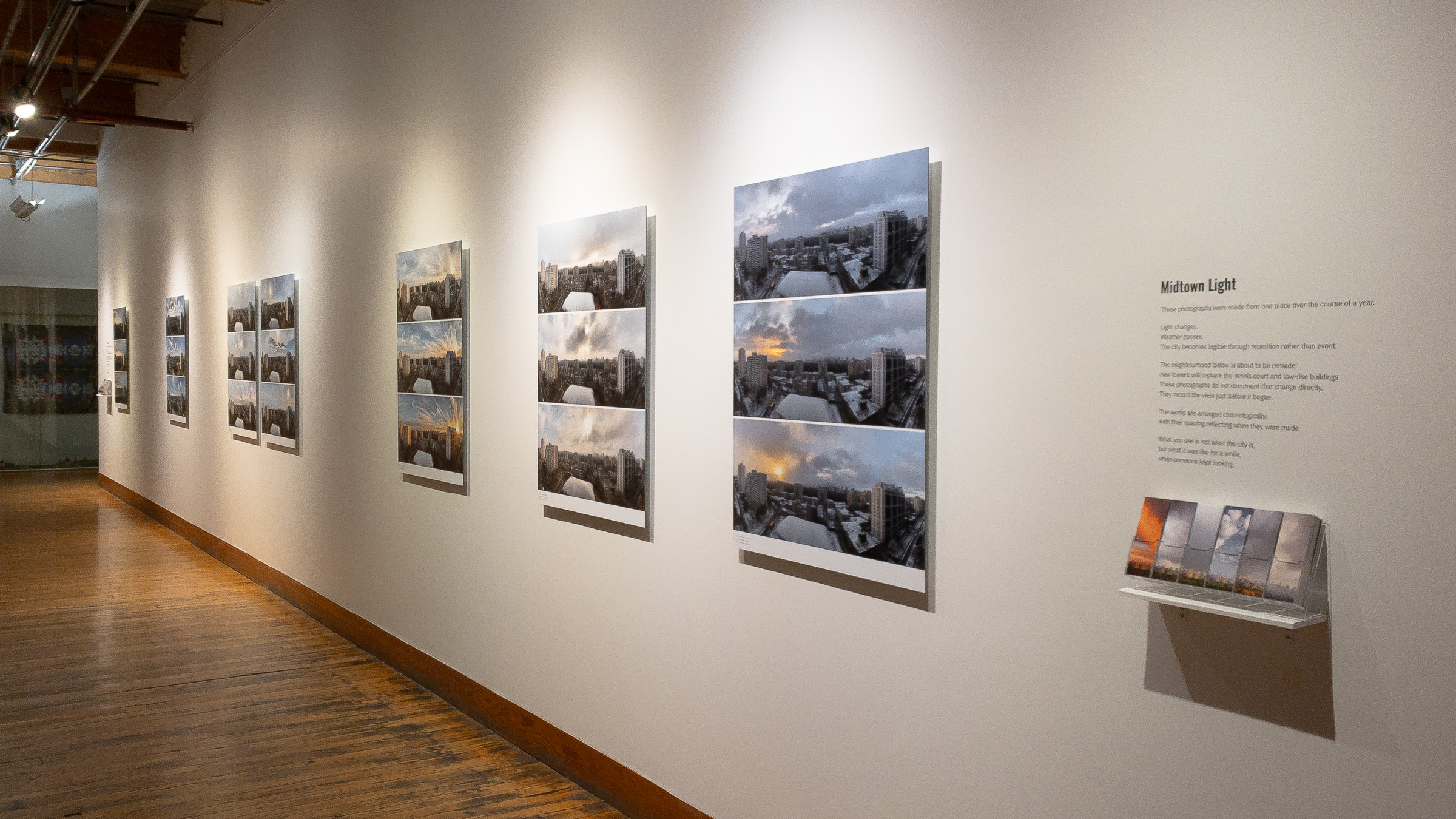 Long view down the exhibition wall, the Shifts receding along the corridor, with the project text and bookmarks at the near end.