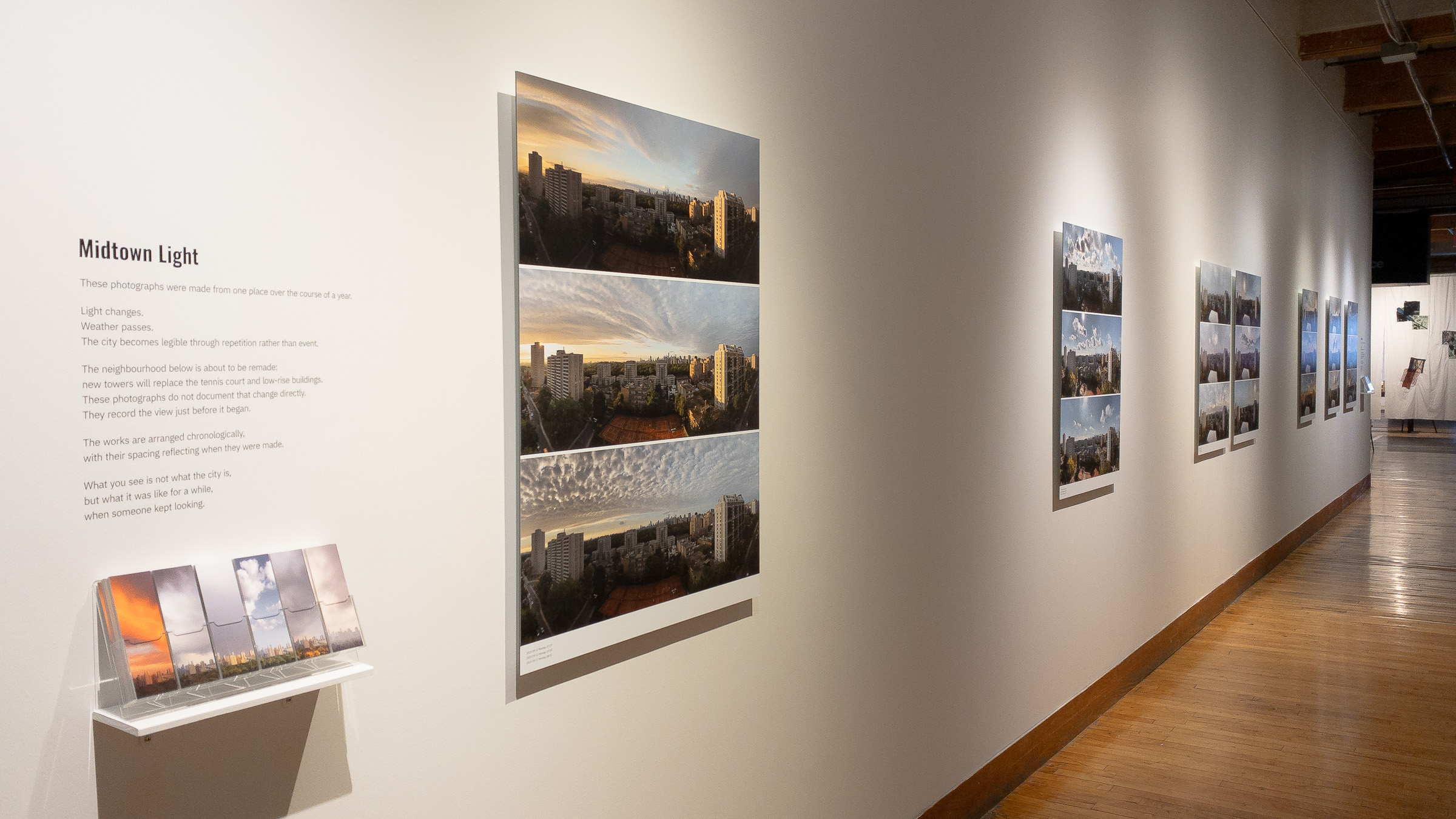 The exhibition corridor at Urbanspace Gallery, with the project text and bookmarks at the near end, the first Shift beside them, and the remaining works receding along the wall.